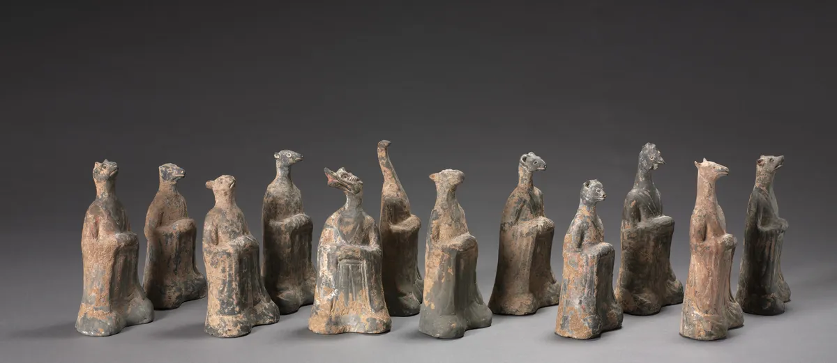 Douze figurines funéraires en terre cuite grise du VIe siècle : des personnages assis à tête d'animal, alignés